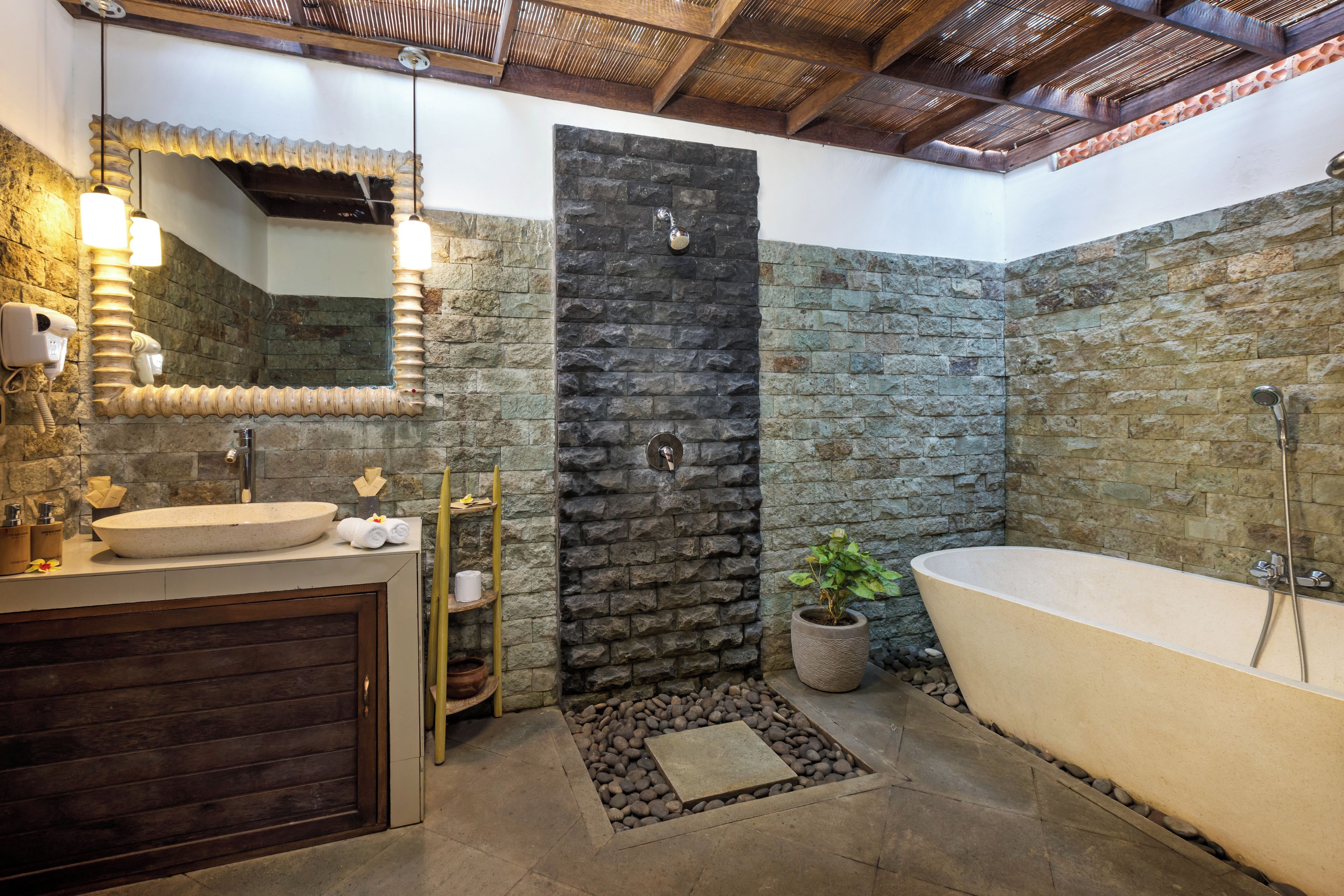 Un baño con pared de piedra, una bañera independiente, un lavabo con espejo y una ducha.