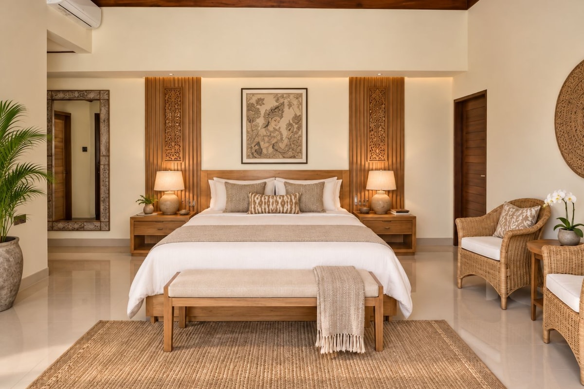 Un dormitorio espacioso con una cama grande, dos mesitas de noche con lámparas, un espejo decorativo y una silla de mimbre con una planta en maceta.