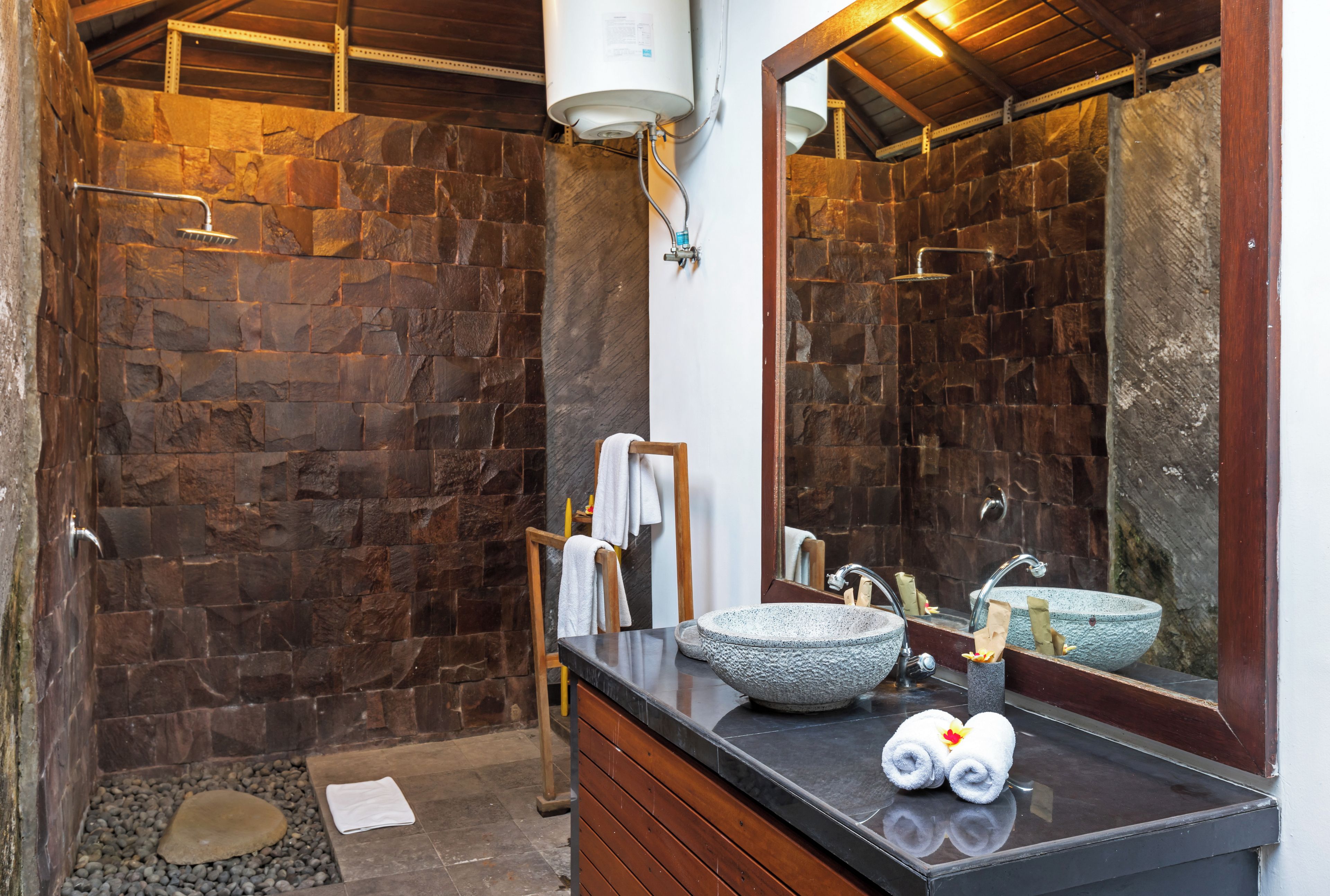 A bathroom with a stone wall, a sink with a stone basin, a mirror, and a towel rack.
