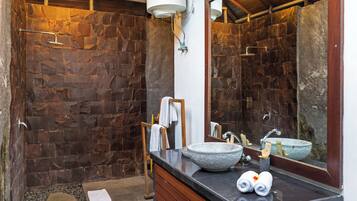 A bathroom with a stone wall, a sink with a stone basin, a mirror, and a towel rack.