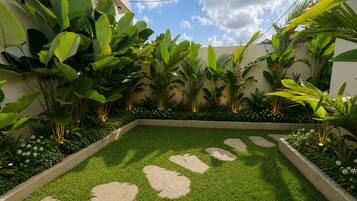 Un giardino curato con erba sintetica, pietre per il cammino e diverse piante tropicali.