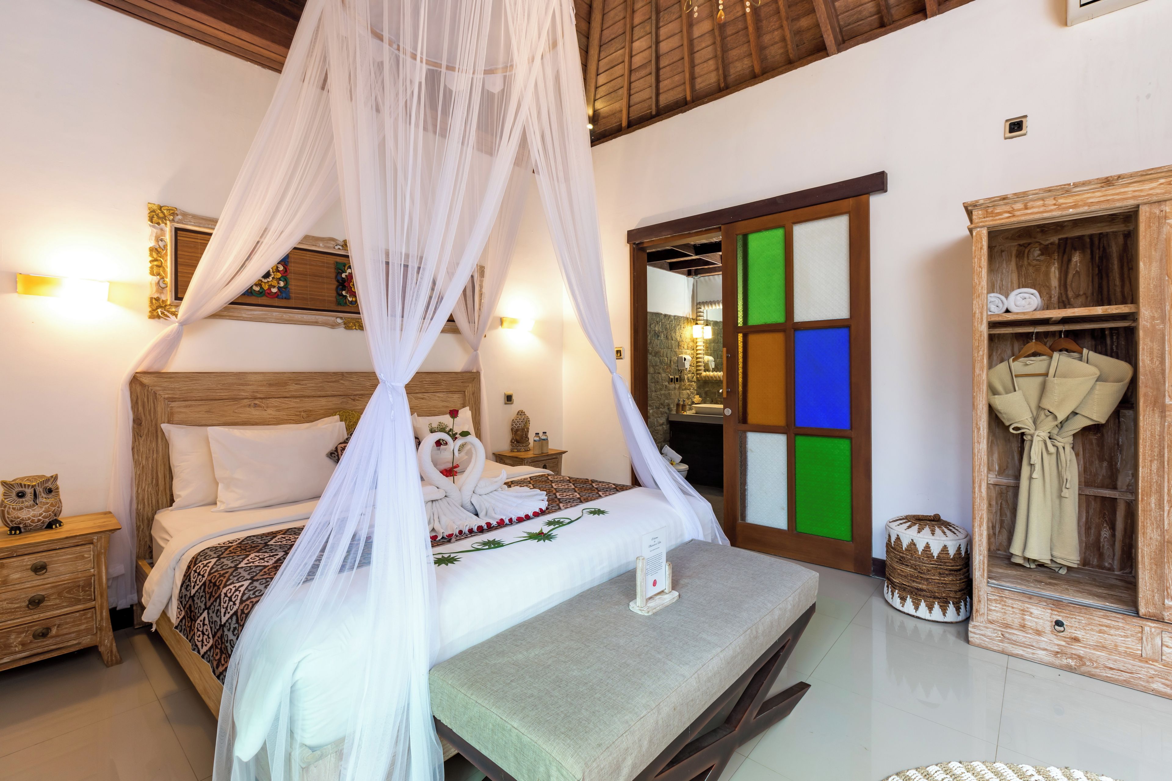 Un dormitorio con cama con dosel, cabecera de madera, mesita de noche con un búho decorativo, una mesita auxiliar y un armario con espejo.
