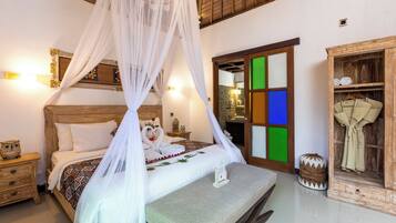 Un dormitorio con cama con dosel, cabecera de madera, mesita de noche con un búho decorativo, una mesita auxiliar y un armario con espejo.