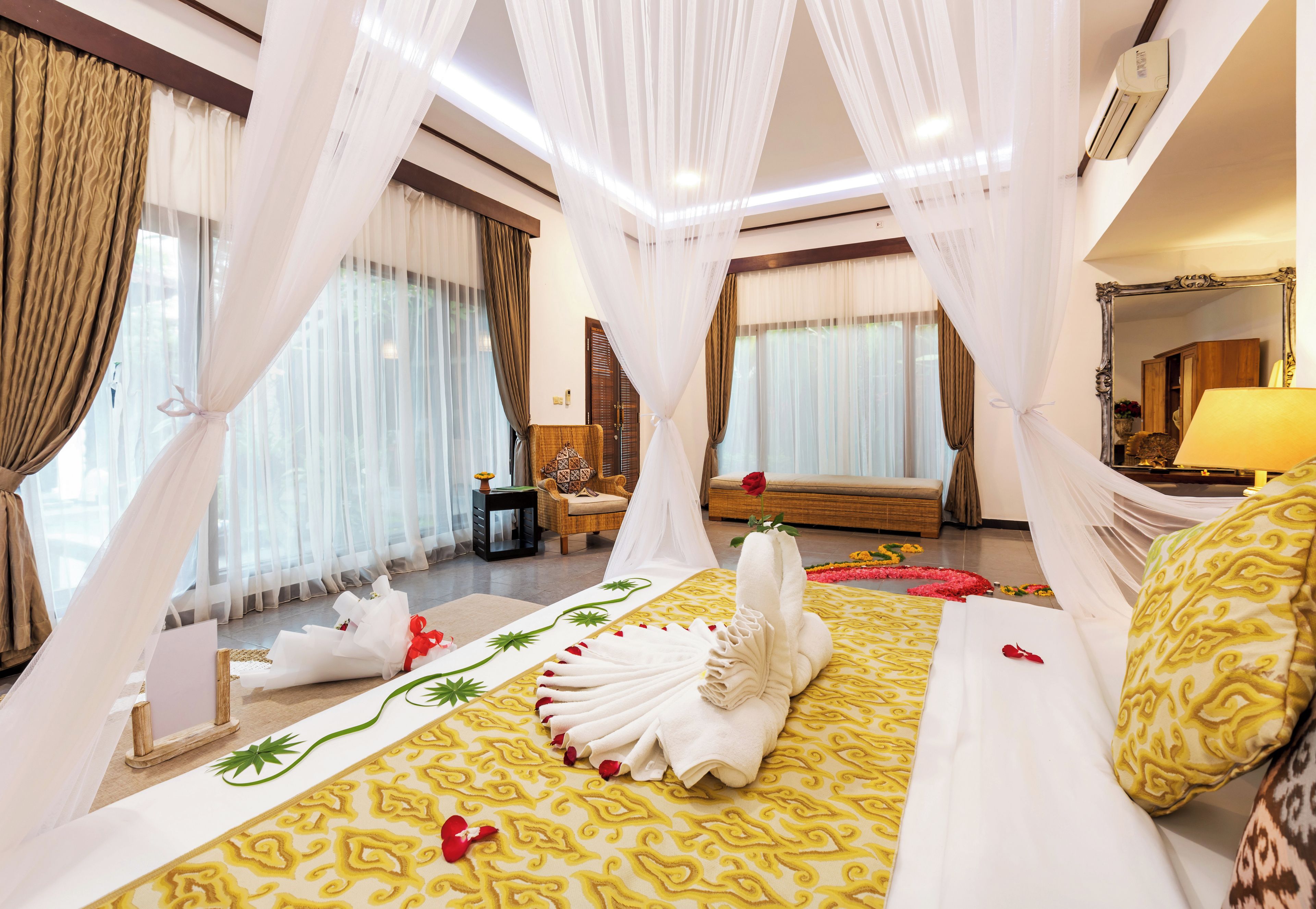 A hotel room with a bed, curtains, a chair, a bedside table, and a mirror.