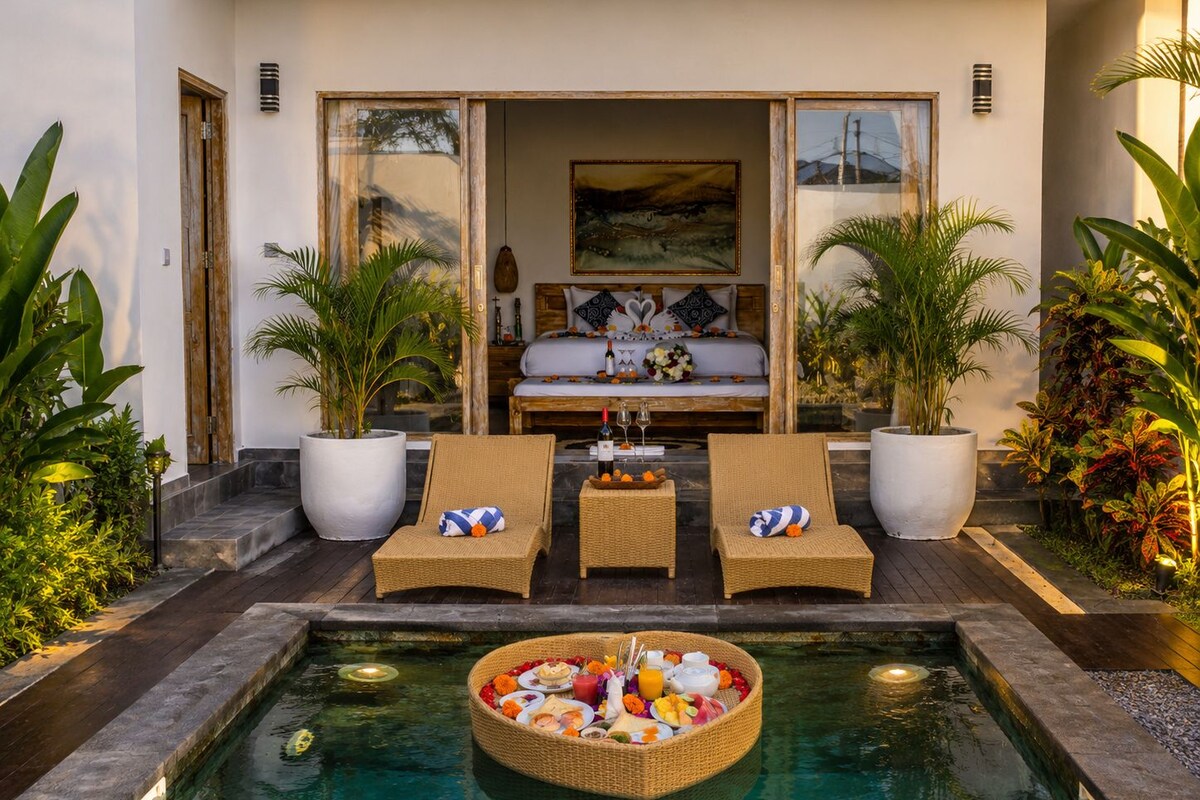 Zona junto a la piscina con comedor, dos sillones de descanso y una habitación con cama y un cuadro.