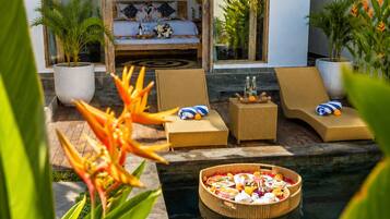 A modern outdoor pool area with lounge chairs, a dining table, and a bed with a view.