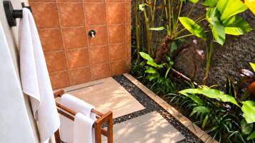 A spa area with a tiled shower, a wooden bench with towels, and a pebbled walkway.