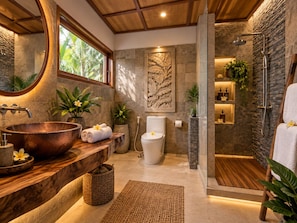 Un baño con tocador de madera, lavamanos de cobre, inodoro, ducha y pared de piedra con un relieve de hoja.