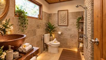 A bathroom with a large copper sink, a toilet, a shower, and a wooden vanity with towels.