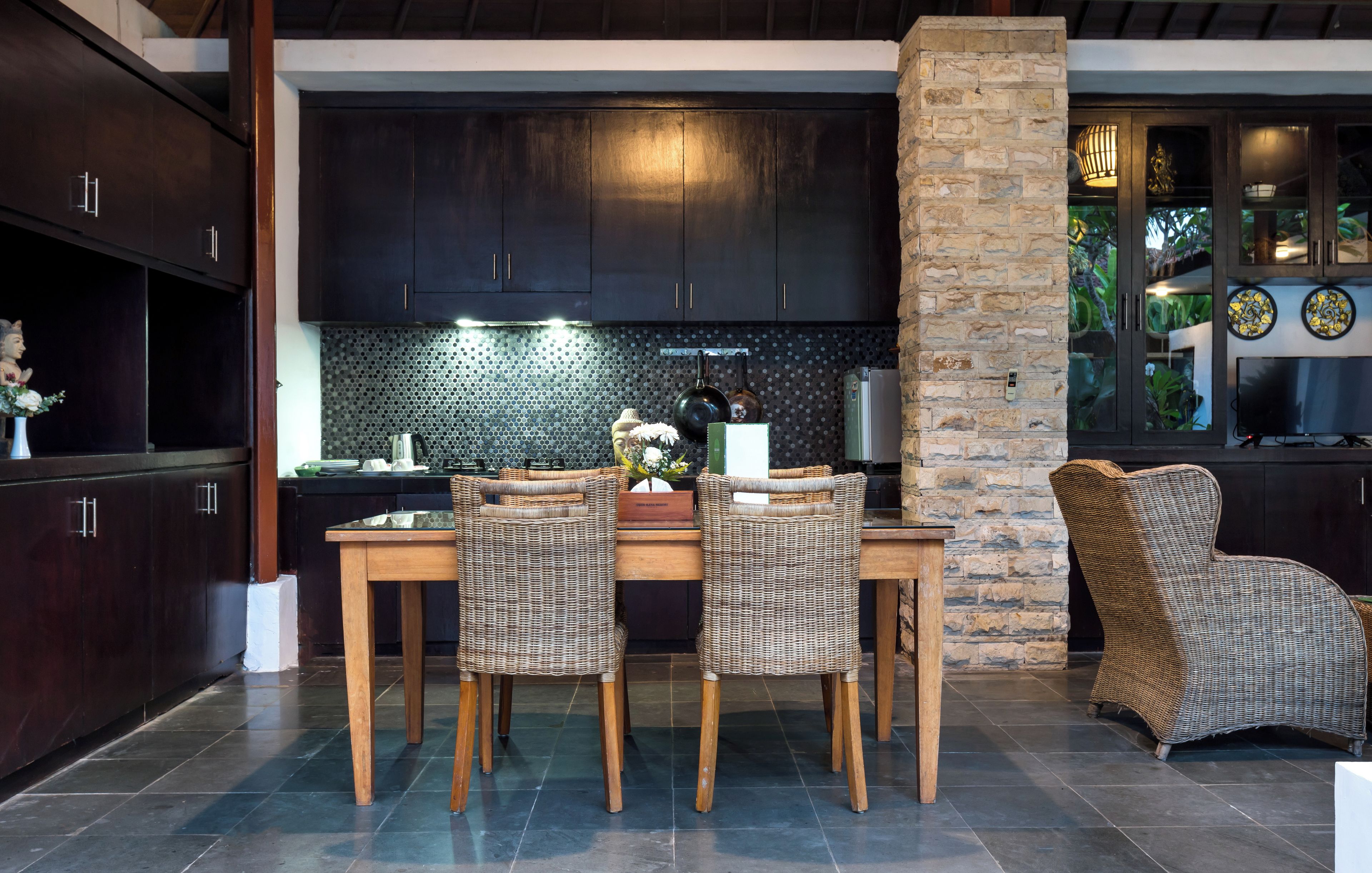 Una cocina moderna con armarios de madera oscura, un pilar de piedra y una zona de comedor con sillas de mimbre y una mesa de madera.