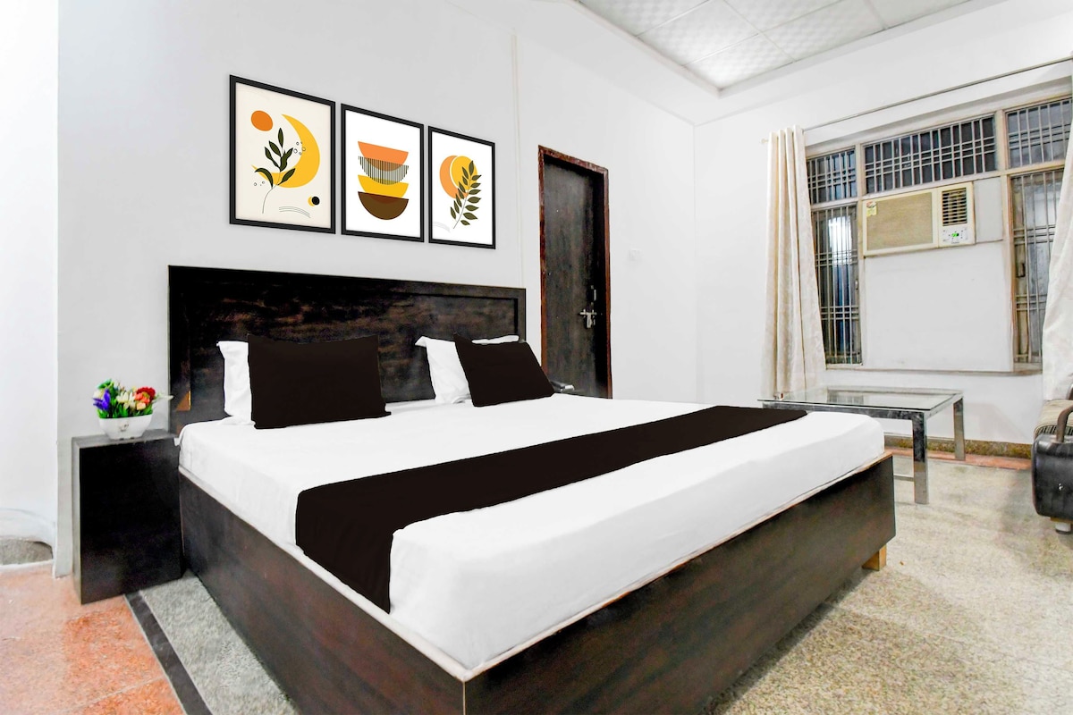 A modern bedroom with a large bed, a bedside table, a small table, and a window with an air conditioning unit.