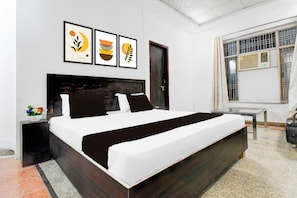 Quarto moderno com cama grande, mesa de cabeceira, mesinha e janela com ar condicionado.