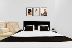 Quarto com cama, uma cadeira e três quadros na parede.