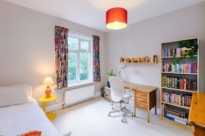 Ein gut beleuchteter Raum mit Schreibtisch, Stuhl, Bücherregal und einem Fenster mit Vorhängen.