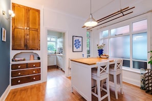 A kitchen with wooden cabinets, a wooden island with chairs, a pendant light, and a window with frosted glass. - Characterful 3BD Townhouse, Manchester (Greater Manchester)