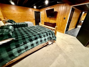 A room with a bed, a television mounted on the wall, and a door leading to another room. - Peaceful Mountain Escape with Deck and Game Room in Jamaica, Vermont (Jamaica)