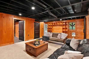 A cozy living room with a leather sofa, a glass coffee table, and wooden paneling. - Peaceful Mountain Escape with Deck and Game Room in Jamaica, Vermont (Jamaica)
