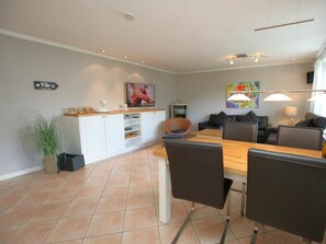 Een moderne woonkamer met een eetgedeelte, witte kasten, een flatscreen televisie en een groot raam.