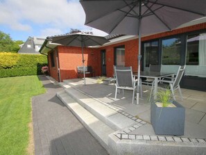 An outdoor patio area with a table and chairs, a large umbrella, and a potted plant. - Schmalstieg 11a, Wyker Perle (Wyk auf Foehr)