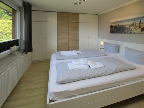 Een slaapkamer met twee bedden, een grote kledingkast, een radiator en een raam met zonwering.