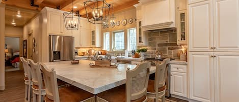 A spacious kitchen with a large island, white cabinetry, and a wooden ceiling.