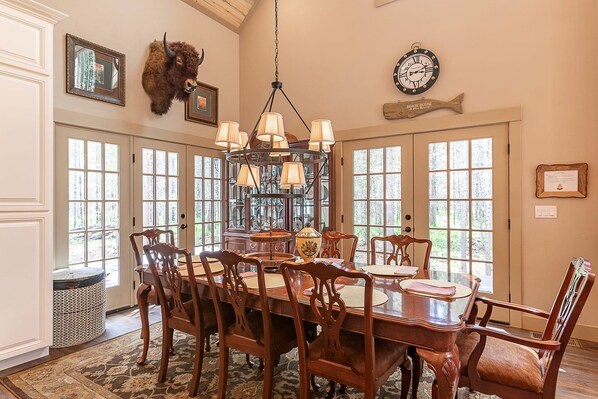 A dining room with a large wooden table, multiple chairs, a chandelier, and a mounted clock. - Secluded Cabin with Scenic Reservoir Access & Trails in Island Park, Idaho (Island Park)