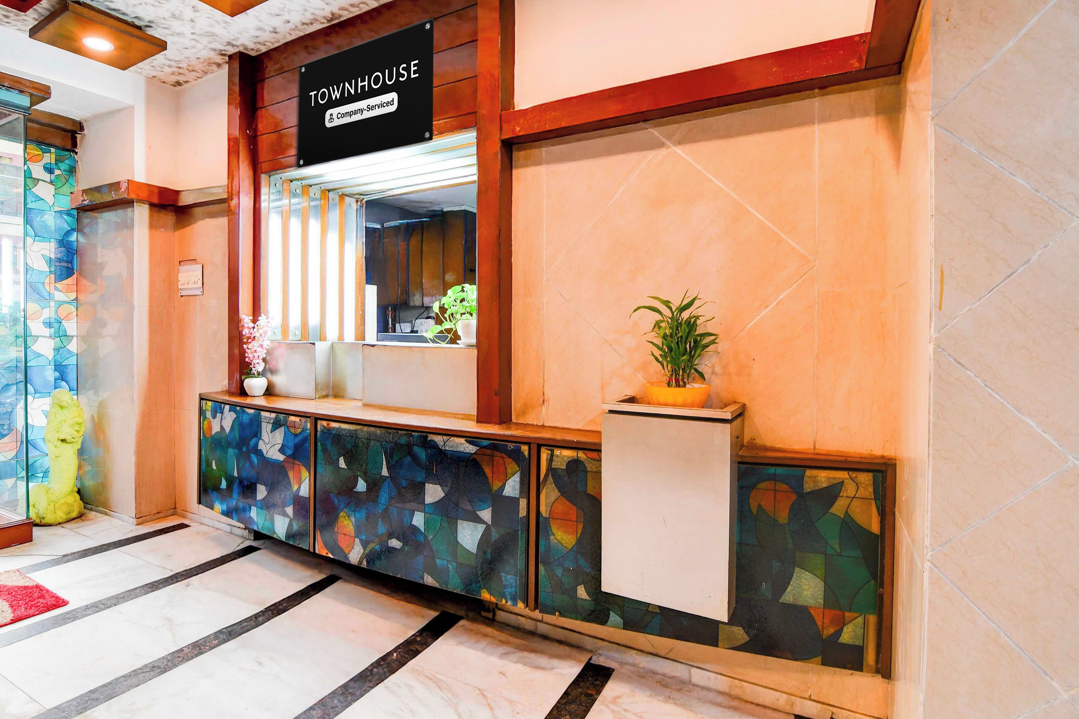 Zona de recepción con un letrero que dice 'TOWNHOUSE', un aviso de la empresa, un mostrador de recepción, una planta en maceta y un ventanal con vidrieras de colores.