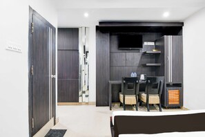 Habitación de hotel con cama, escritorio con dos sillas, televisión y pequeña zona de kitchenette.