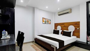 A modern hotel room with a large bed, a wooden headboard, a desk with a chair, and an air conditioning unit. - Townhouse Kolkata Northern Park (Kolkata)
