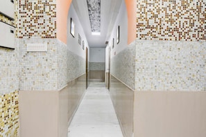 Un pasillo con paredes de azulejos y suelo de mármol, que conduce a una puerta al final.