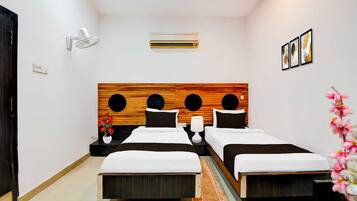 Habitación de hotel con dos camas, cabecera de madera, aire acondicionado instalado en la pared, mesita de noche con lámpara y un pequeño florero con flores.