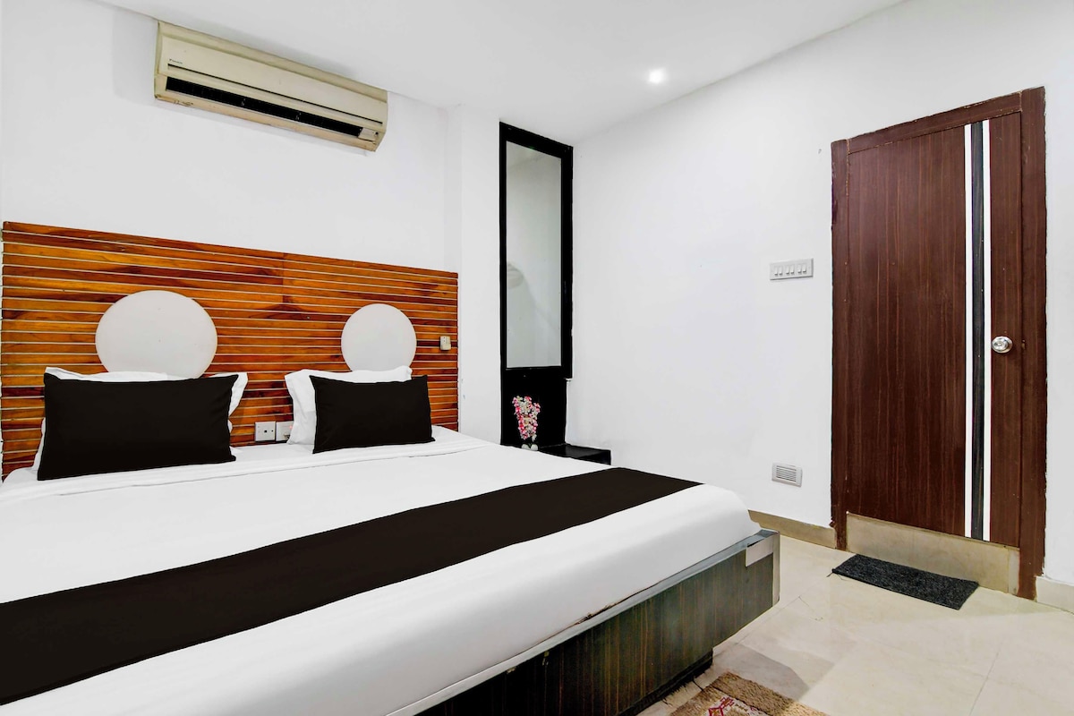 Habitación de hotel con cama, cabecera de madera, espejo, puerta y aire acondicionado de pared.