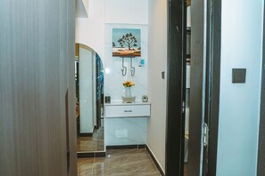 A hallway with a marble floor, a white wall with a framed picture, a small white cabinet with a vase of flowers, and a door with a black frame. - Cozy 1-bedroom apartment with gym, swimming pool in fabulous Nairobi Lavington (Nairobi)