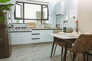 A modern kitchen with a dining area, a view of buildings outside, and a vase with a flower on the table. - Cozy 1-bedroom apartment with gym, swimming pool in fabulous Nairobi Lavington (Nairobi)