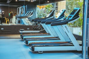 Eine Reihe stehender Fitnessräder in einem Fitnessstudio mit einer Glaswand, durch die man nach draußen blicken kann.