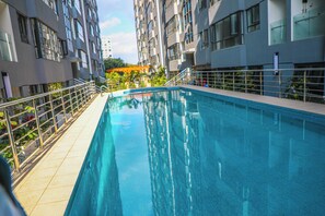Ein Schwimmbecken mit gefliestem Sonnendeck und Metallgeländern, umgeben von modernen Gebäuden mit Balkonen.