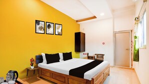 A hotel room with a bed, a bedside table with a kettle and cups, a small cabinet, and a door with a curtain. - Townhouse Kolkata Padmapukur Lake (Kolkata)