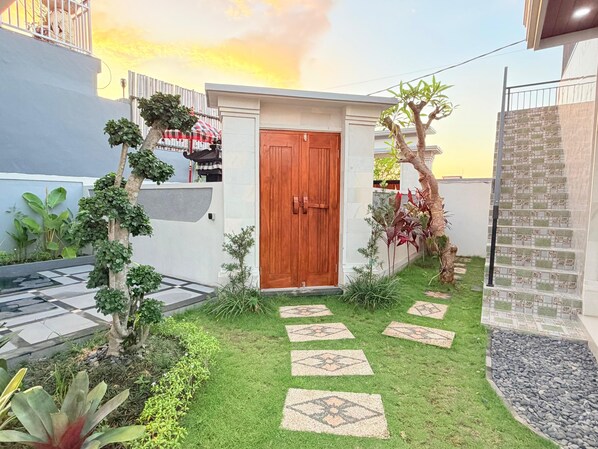 A residential property with a wooden door, a small garden with stepping stones, and a tiled wall. - Villa Romansa Lovina (Buleleng)