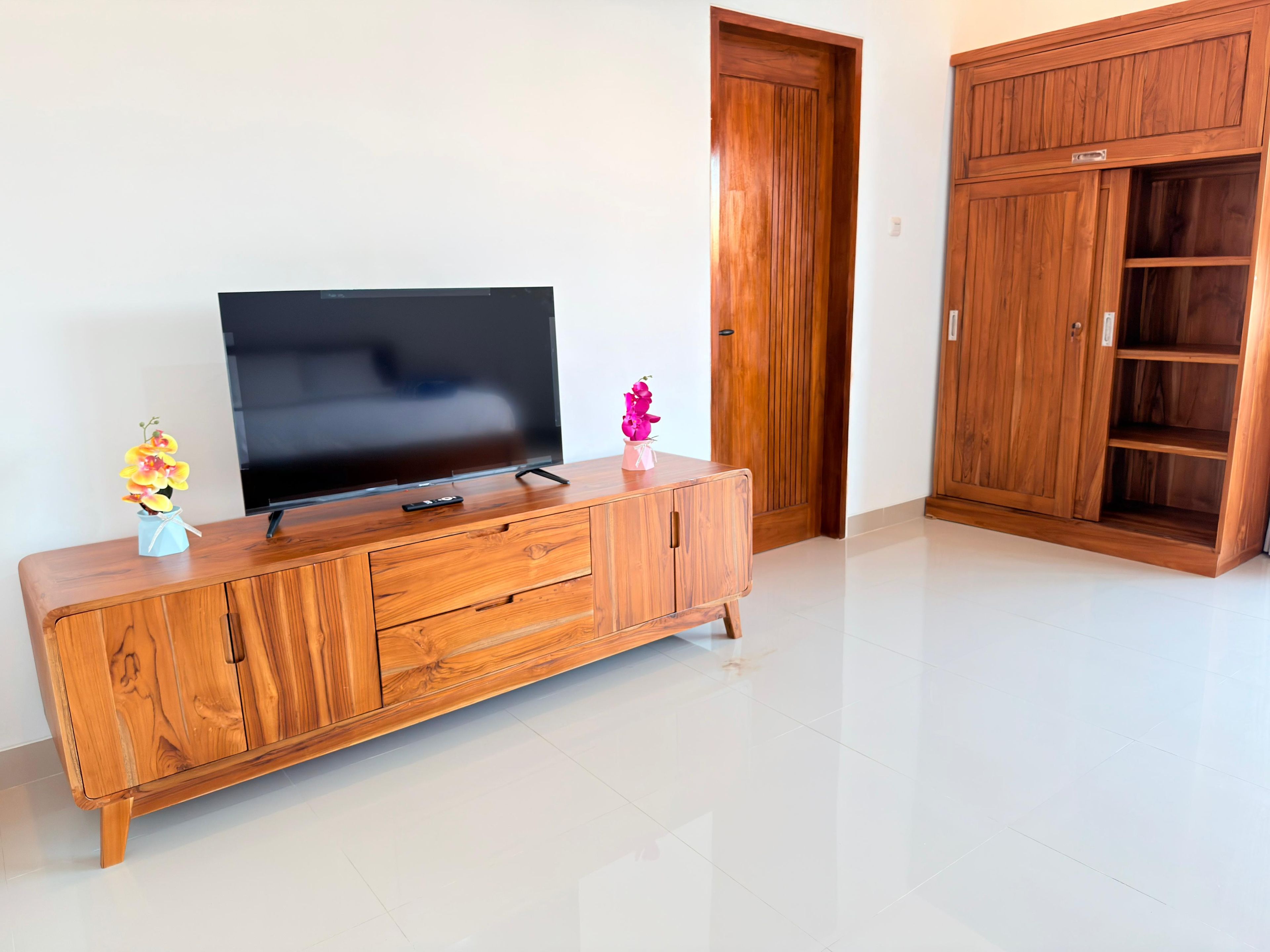 Een houten tv-meubel met een flatscreen televisie, een kleine vaas met bloemen en een roze decoratie.