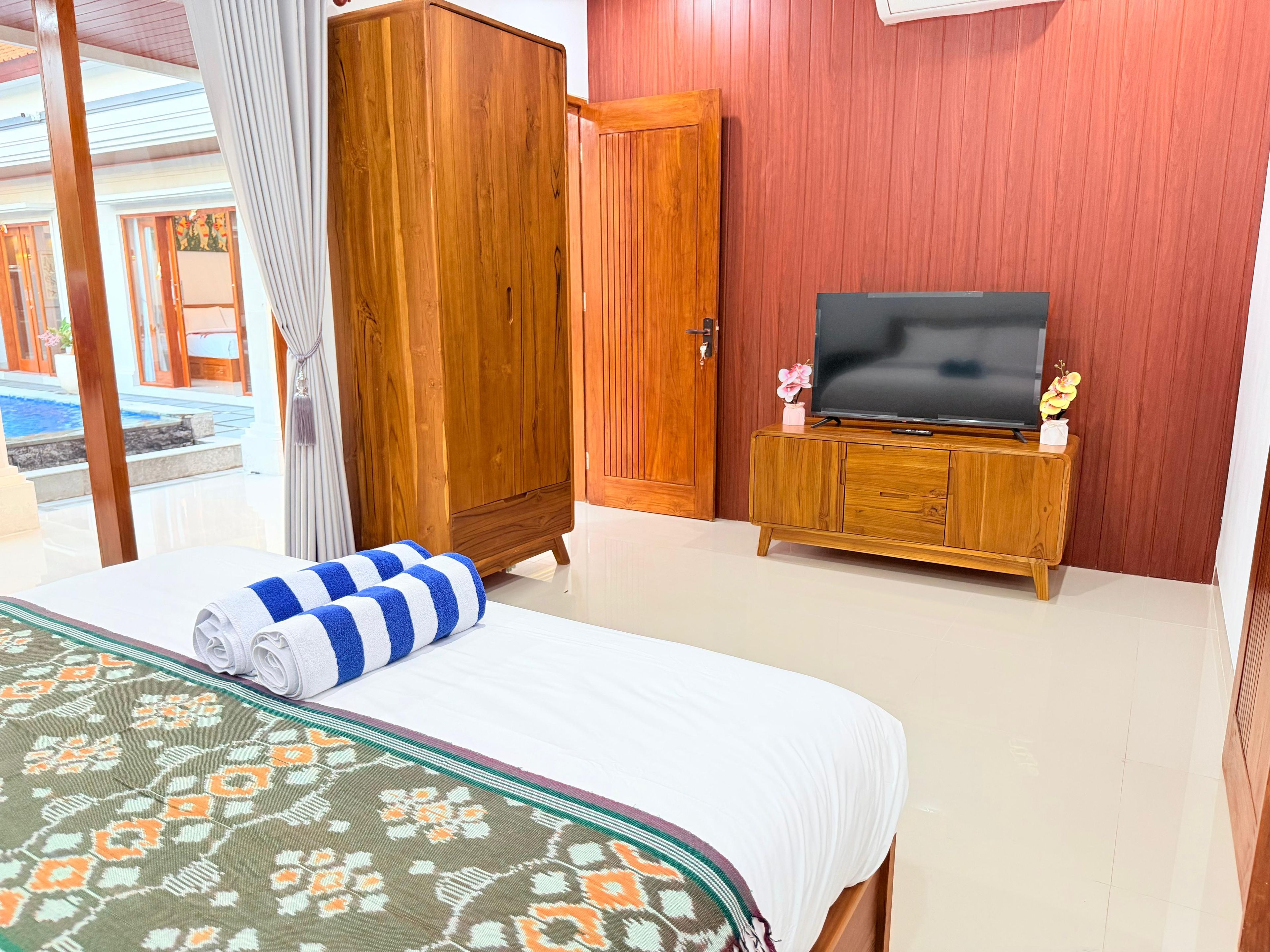 Habitación de hotel con cama, televisor sobre un mueble de madera y vista a una piscina.