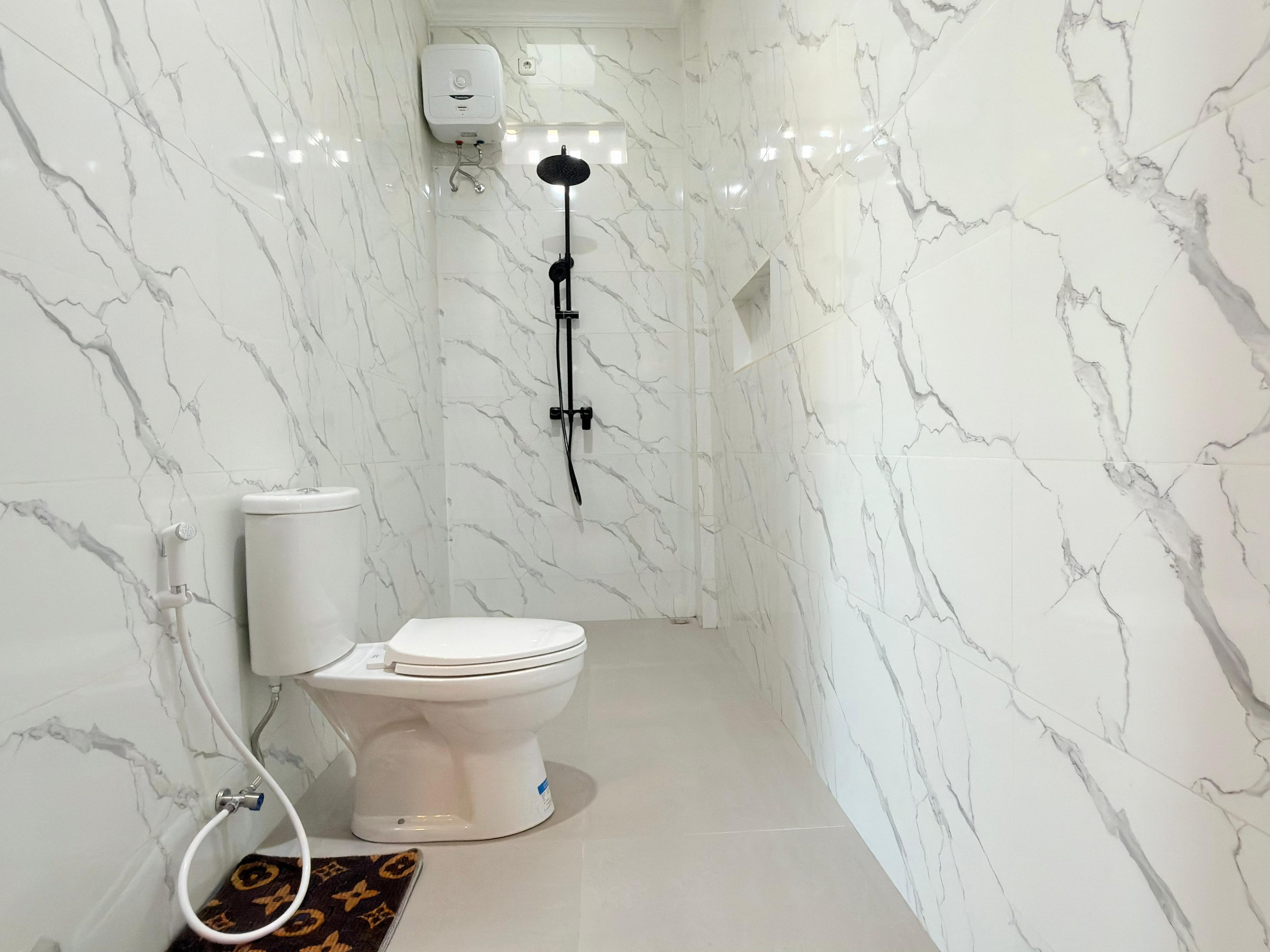 Un baño con inodoro, ducha y pared de mármol.