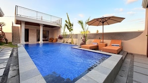 Une piscine avec des chaises longues et un parasol, entourée d’un bâtiment doté d’un balcon.