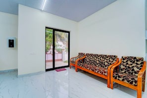 Una habitación amplia con piso de mármol, un conjunto de sofás, una puerta de vidrio corrediza que da al exterior y un enchufe de pared.