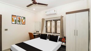 A hotel room with a bed, a desk, a chair, a wardrobe, a ceiling fan, and a window with curtains. - Townhouse Birsa Railway Stadium Ranchi (Ranchi)
