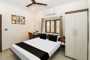 Habitación de hotel con cama, escritorio, silla, armario, ventilador de techo y ventana con cortinas.