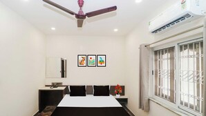 A hotel room with a bed, bedside tables, a ceiling fan, an air conditioning unit, a window with bars, and three framed artworks on the wall. - Townhouse Birsa Railway Stadium Ranchi (Ranchi)