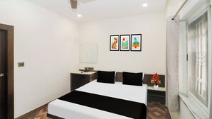 A hotel room with a bed, a bedside table, a nightstand, a ceiling fan, a window with curtains, and wall art. - Townhouse Birsa Railway Stadium Ranchi (Ranchi)