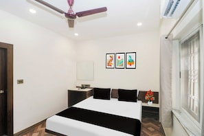 Habitación de hotel con cama, mesita de noche, ventilador de techo, ventana con cortinas y decoración en la pared.