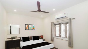 A hotel room with a bed, bedside table, mirror, artwork, window with bars, ceiling fan, and air conditioning unit. - Townhouse Birsa Railway Stadium Ranchi (Ranchi)