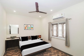 Habitación de hotel con cama, mesita de noche, espejo, obra de arte, ventana con rejas, ventilador de techo y aire acondicionado.